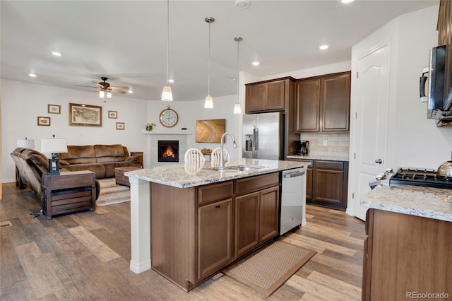 kitchen with stainless steel appliances, a sink, light wood-style floors, a ceiling fan, and decorative backsplash