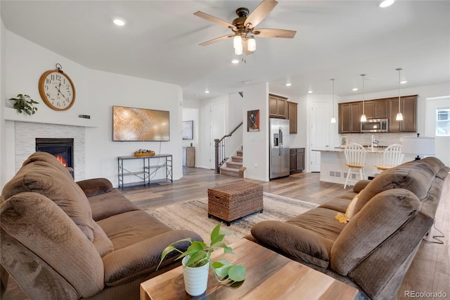 living room featuring ceiling fan, recessed lighting, light wood-style flooring, a fireplace, and stairway