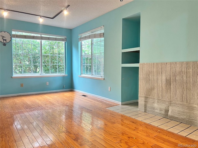 unfurnished room with a textured ceiling, light wood-type flooring, visible vents, and baseboards