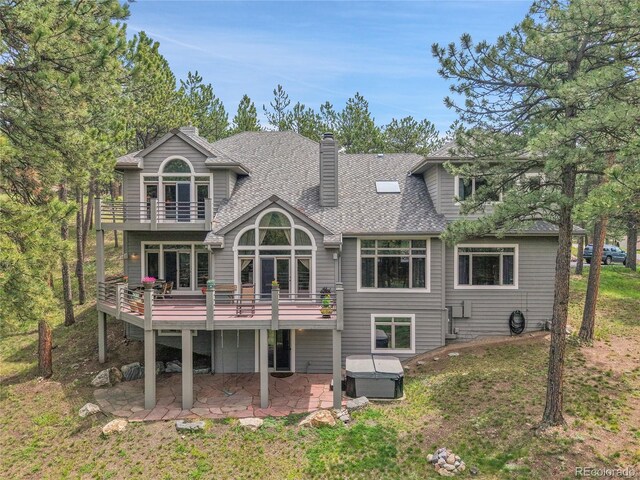 29433 Firethorne Ct, Evergreen, CO 80439 - back of house with a balcony, a hot tub, a patio area, a shingled roof, and a chimney