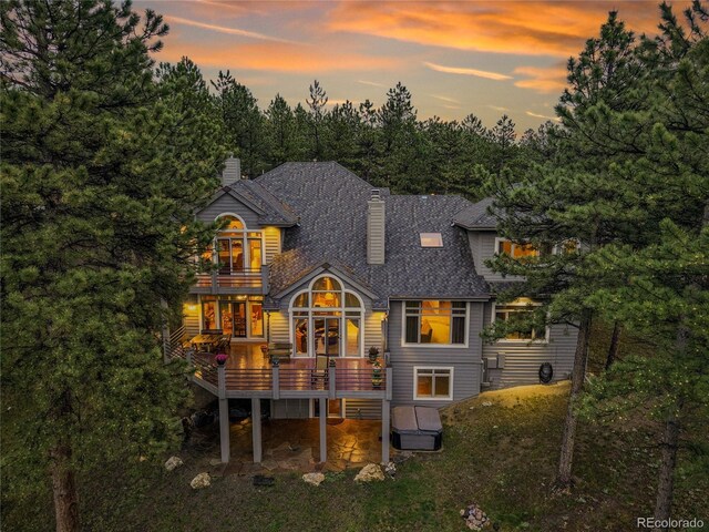 29433 Firethorne Ct, Evergreen, CO 80439 - back of house at dusk with a balcony, a chimney, a deck, a patio area, and a shingled roof