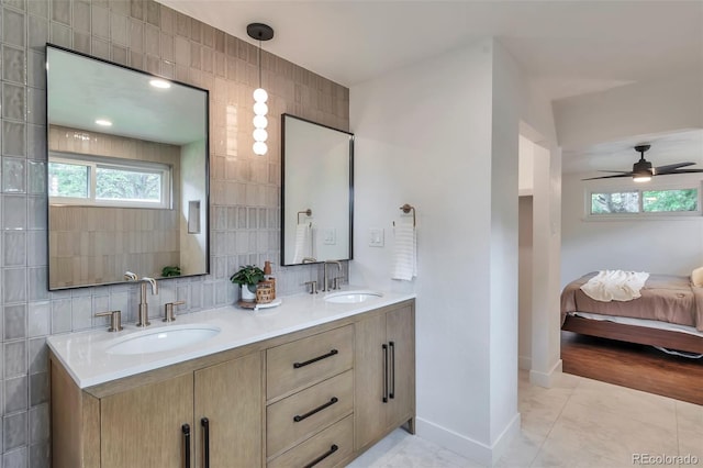 2598 Teller St, Lakewood, CO 80214 - ensuite bathroom featuring double vanity, tile patterned flooring, tile walls, a ceiling fan, and decorative backsplash