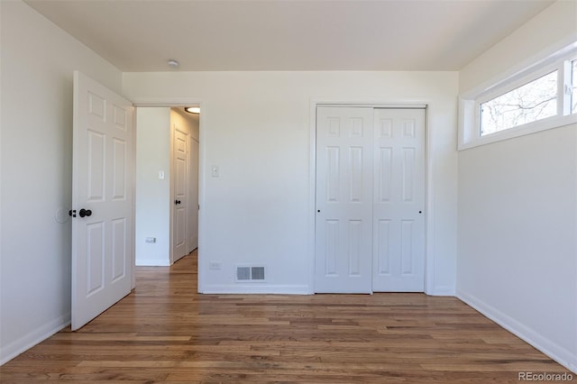 unfurnished bedroom with visible vents, baseboards, wood finished floors, and a closet