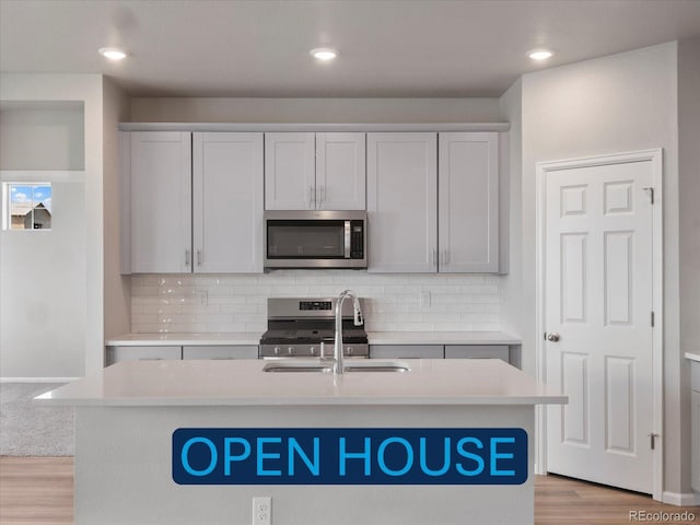 kitchen featuring sink, a kitchen island with sink, stainless steel appliances, and light wood-type flooring