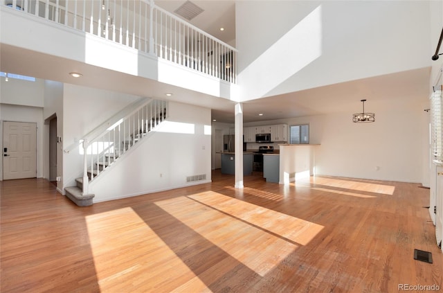 unfurnished living room featuring a high ceiling, a notable chandelier, and light wood-type flooring