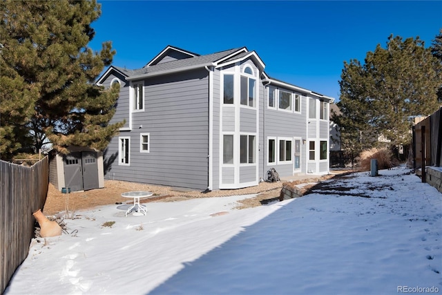 snow covered back of property featuring a storage unit