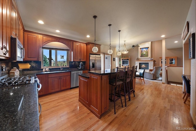 kitchen with a tiled fireplace, a kitchen island, light hardwood / wood-style floors, appliances with stainless steel finishes, and pendant lighting