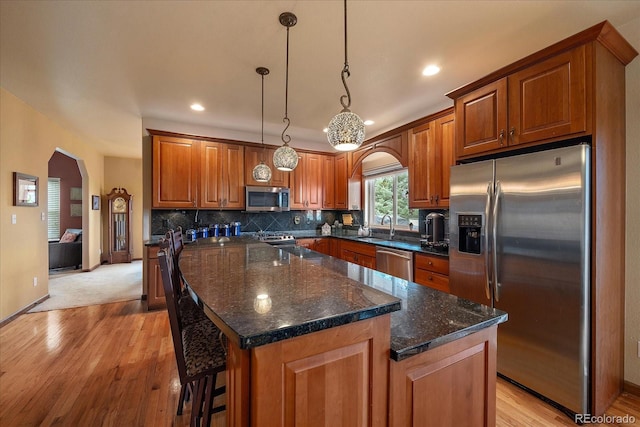 kitchen featuring light carpet, stainless steel appliances, dark stone countertops, hanging light fixtures, and sink