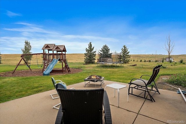 view of patio with a playground, a rural view, a trampoline, and an outdoor fire pit