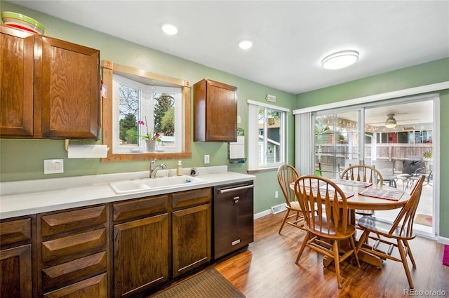 kitchen with a sink, light countertops, stainless steel dishwasher, and wood finished floors