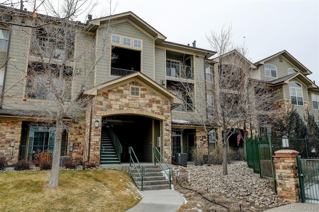 view of front facade with a front yard, stone siding, fence, and central AC unit