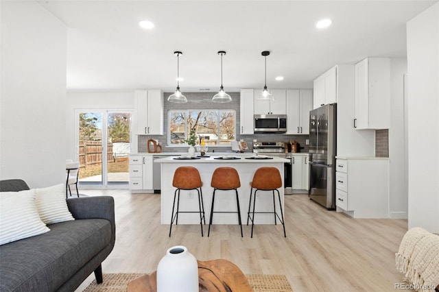 kitchen with a kitchen bar, light wood-style flooring, backsplash, stainless steel appliances, and light countertops