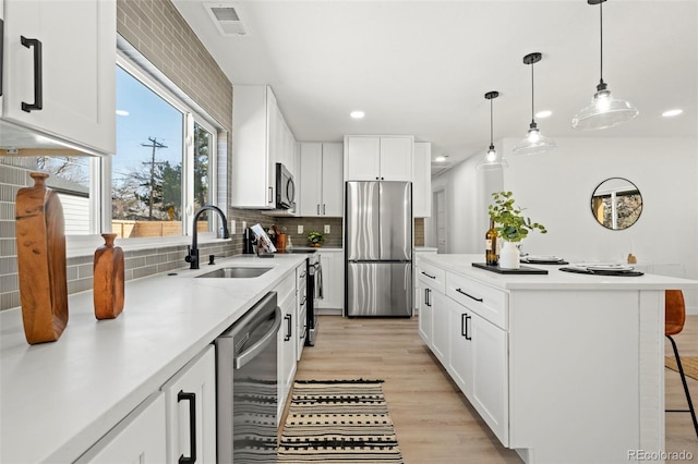 kitchen featuring tasteful backsplash, light countertops, light wood-style floors, stainless steel appliances, and a sink