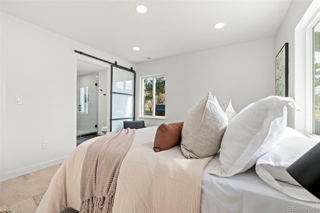 bedroom with wood finished floors, visible vents, baseboards, recessed lighting, and a barn door