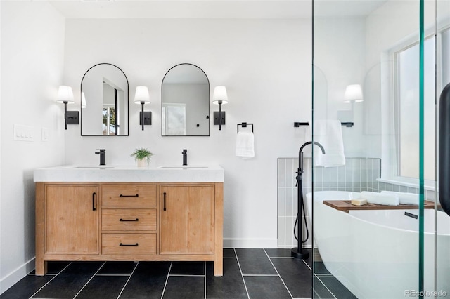 full bathroom featuring baseboards, a freestanding bath, double vanity, tile patterned floors, and a sink