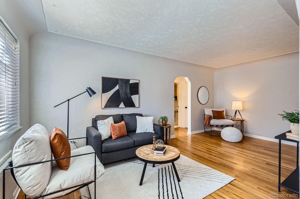 living area featuring light wood-type flooring, baseboards, arched walkways, and a textured ceiling