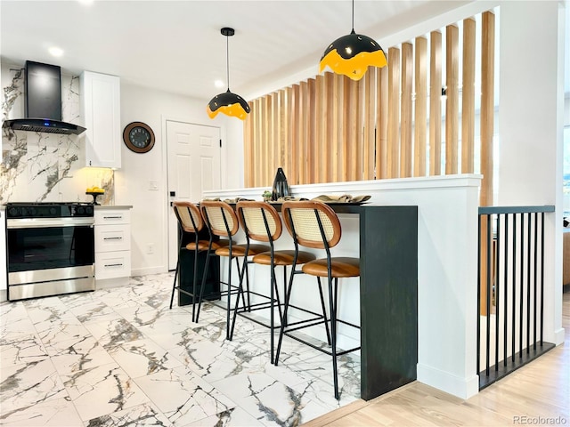 kitchen with gas stove, white cabinets, backsplash, and wall chimney exhaust hood