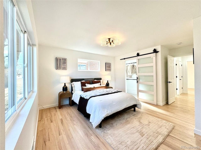 bedroom featuring light wood-type flooring, a barn door, and baseboards