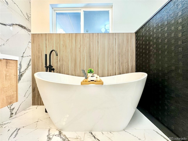 bathroom featuring marble finish floor and a freestanding tub