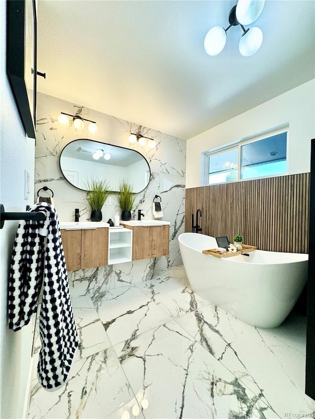 full bath with stone wall, a freestanding tub, tile walls, marble finish floor, and double vanity