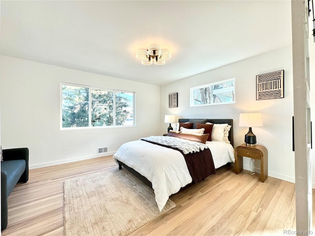 bedroom with light wood-type flooring, visible vents, baseboards, and a notable chandelier