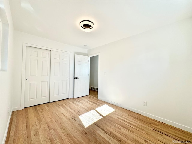 unfurnished bedroom featuring baseboards, light wood-style flooring, visible vents, and a closet