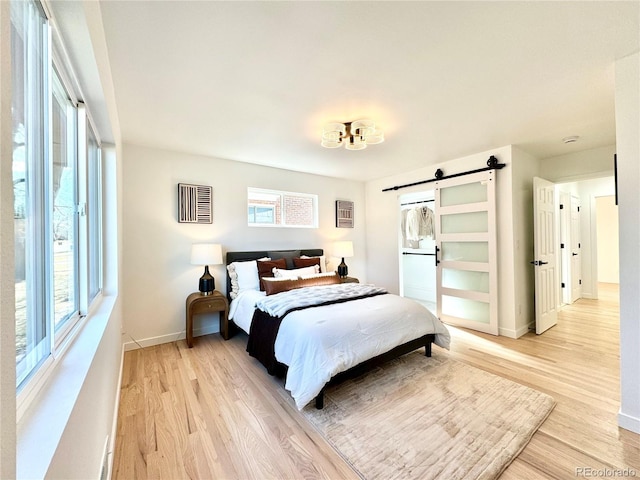 bedroom featuring a barn door, baseboards, visible vents, and light wood-type flooring