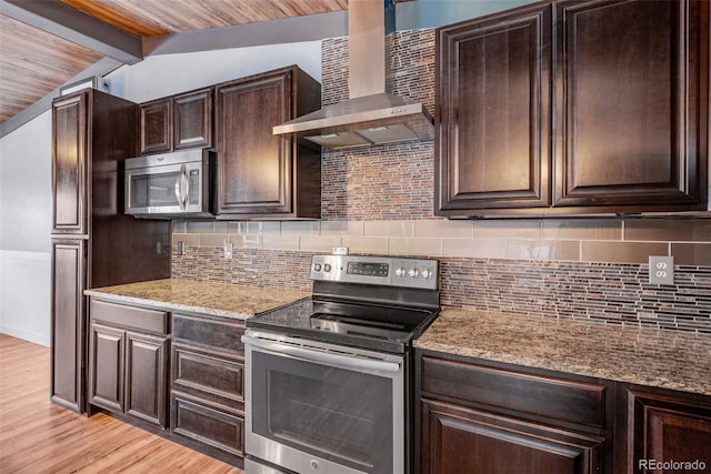 kitchen with appliances with stainless steel finishes, backsplash, wall chimney exhaust hood, lofted ceiling with beams, and light hardwood / wood-style flooring