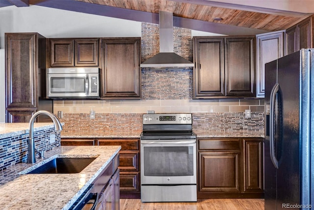 kitchen with wall chimney range hood, sink, stainless steel appliances, and lofted ceiling