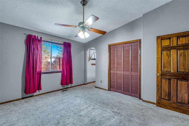 unfurnished bedroom with light carpet, a textured ceiling, vaulted ceiling, ceiling fan, and a closet