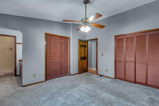 unfurnished bedroom featuring multiple closets, ceiling fan, ensuite bathroom, a textured ceiling, and light carpet