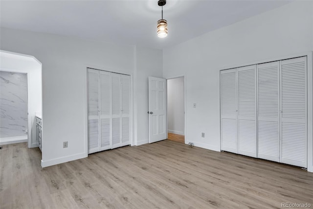 unfurnished bedroom featuring lofted ceiling, two closets, light wood-type flooring, and ensuite bath