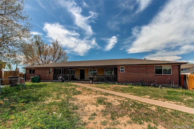 view of front of property featuring fence, a porch, a front lawn, and brick siding