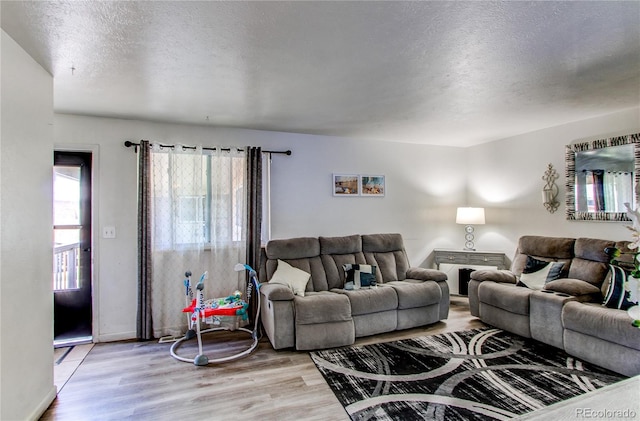 living area featuring a textured ceiling, baseboards, and light wood finished floors