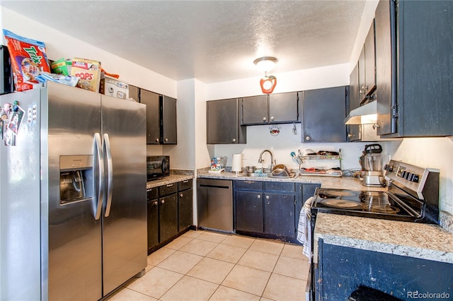 kitchen featuring a textured ceiling, under cabinet range hood, a sink, light tile patterned floors, and stainless steel appliances