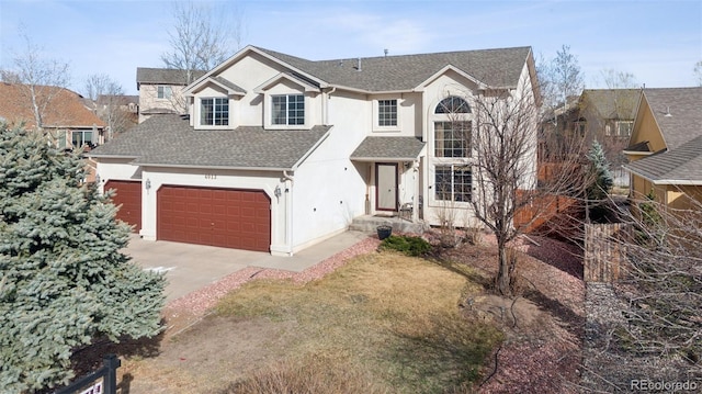 traditional-style home featuring driveway, an attached garage, roof with shingles, and stucco siding