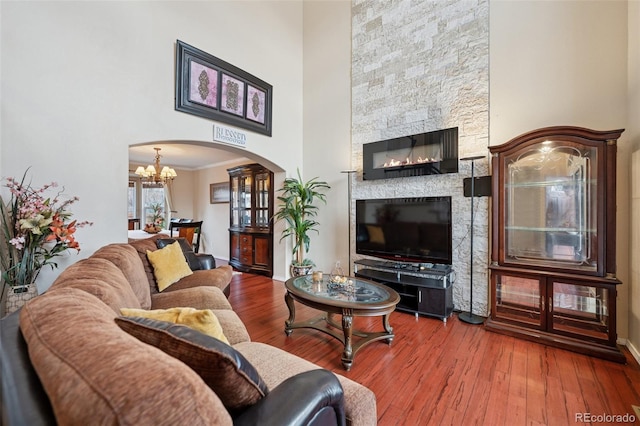 living area featuring crown molding, wood finished floors, arched walkways, a high ceiling, and a notable chandelier