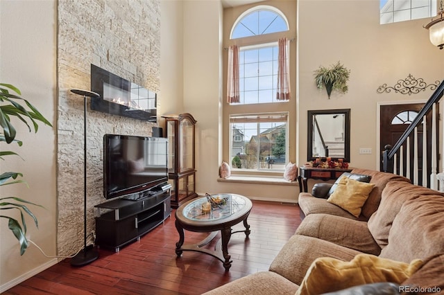 living room featuring hardwood / wood-style floors, stairs, a towering ceiling, and baseboards