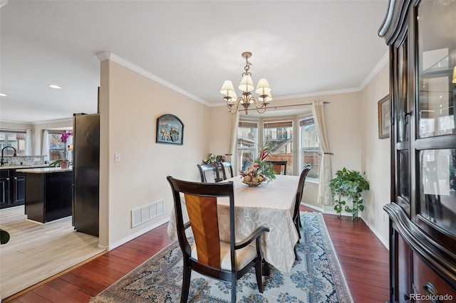 dining room featuring hardwood / wood-style floors, crown molding, visible vents, and a notable chandelier