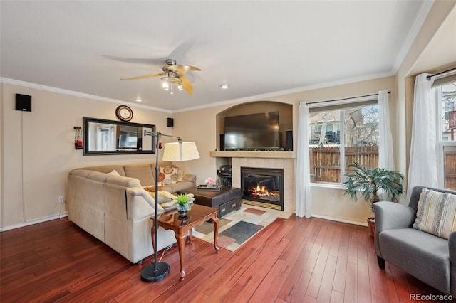 living area with crown molding, baseboards, a ceiling fan, a fireplace, and wood finished floors