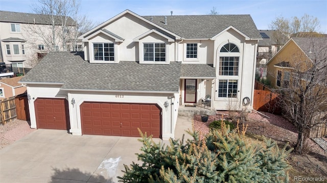 traditional-style home featuring driveway, stucco siding, fence, and roof with shingles