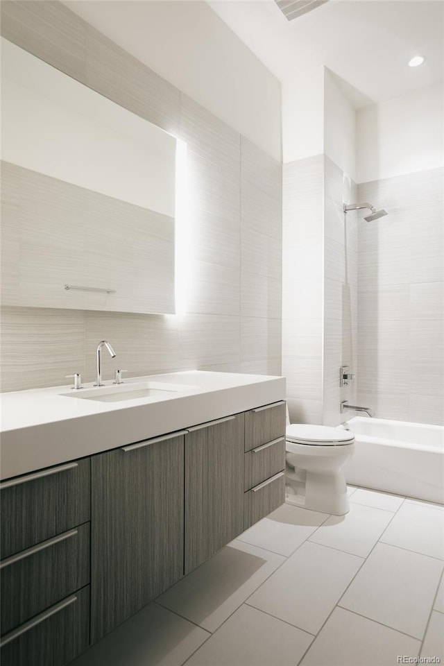 full bathroom with tile flooring, tile walls, tiled shower / bath combo, vanity, and toilet