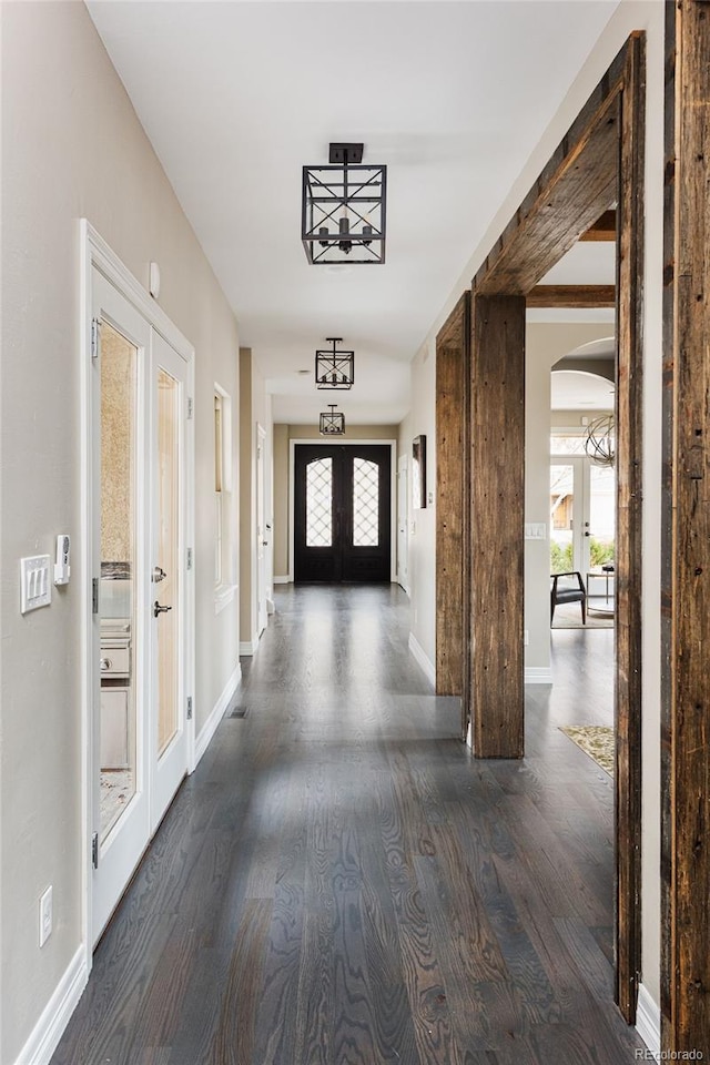 hallway featuring arched walkways, plenty of natural light, dark wood finished floors, and french doors