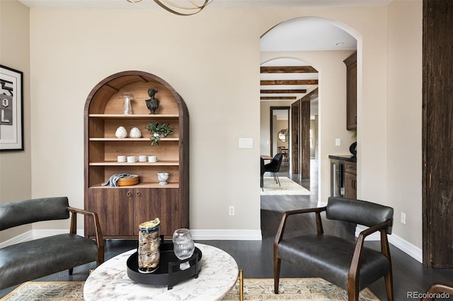 interior space featuring dark wood finished floors, built in shelves, arched walkways, and baseboards