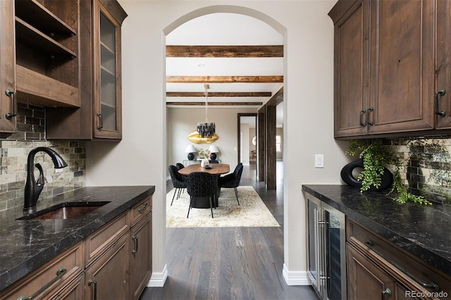 kitchen with beamed ceiling, a sink, dark wood-style floors, dark stone counters, and wine cooler