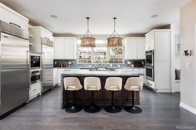 kitchen with a kitchen island, a breakfast bar, decorative backsplash, stainless steel appliances, and white cabinetry