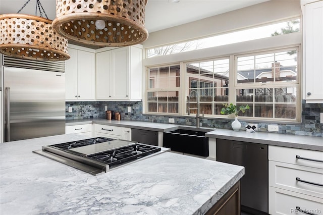 kitchen with backsplash, light stone counters, white cabinets, stainless steel appliances, and a sink