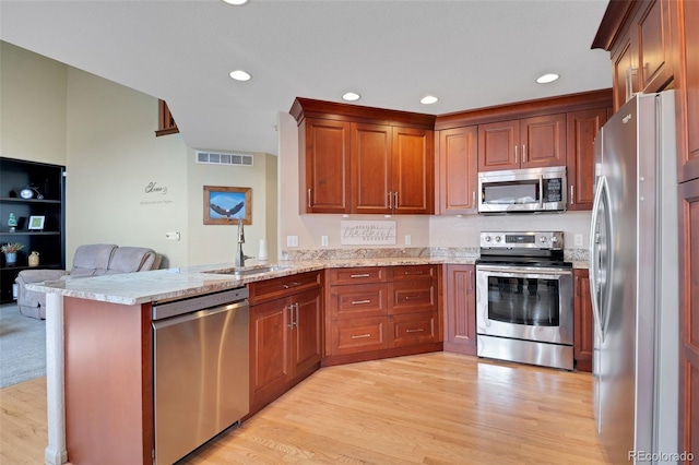 kitchen featuring a peninsula, visible vents, appliances with stainless steel finishes, light wood finished floors, and a sink