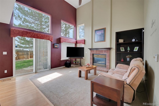 living area featuring a fireplace, visible vents, a high ceiling, and wood finished floors
