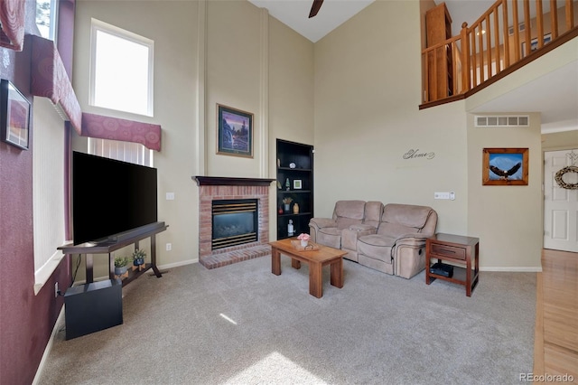 carpeted living room with visible vents, a brick fireplace, a towering ceiling, and baseboards